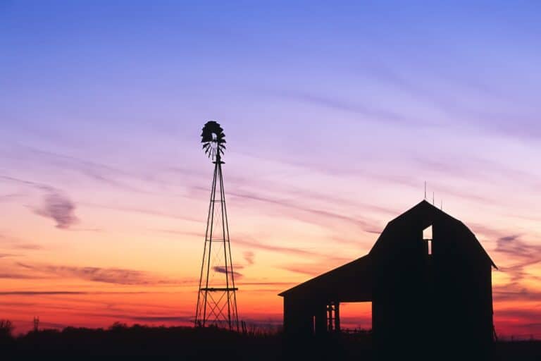 Silhouette of barn and windmill against sunset