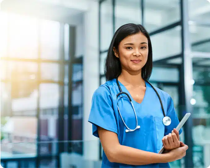 Young nurse wearing stethoscope and carrying tablet in hospital setting