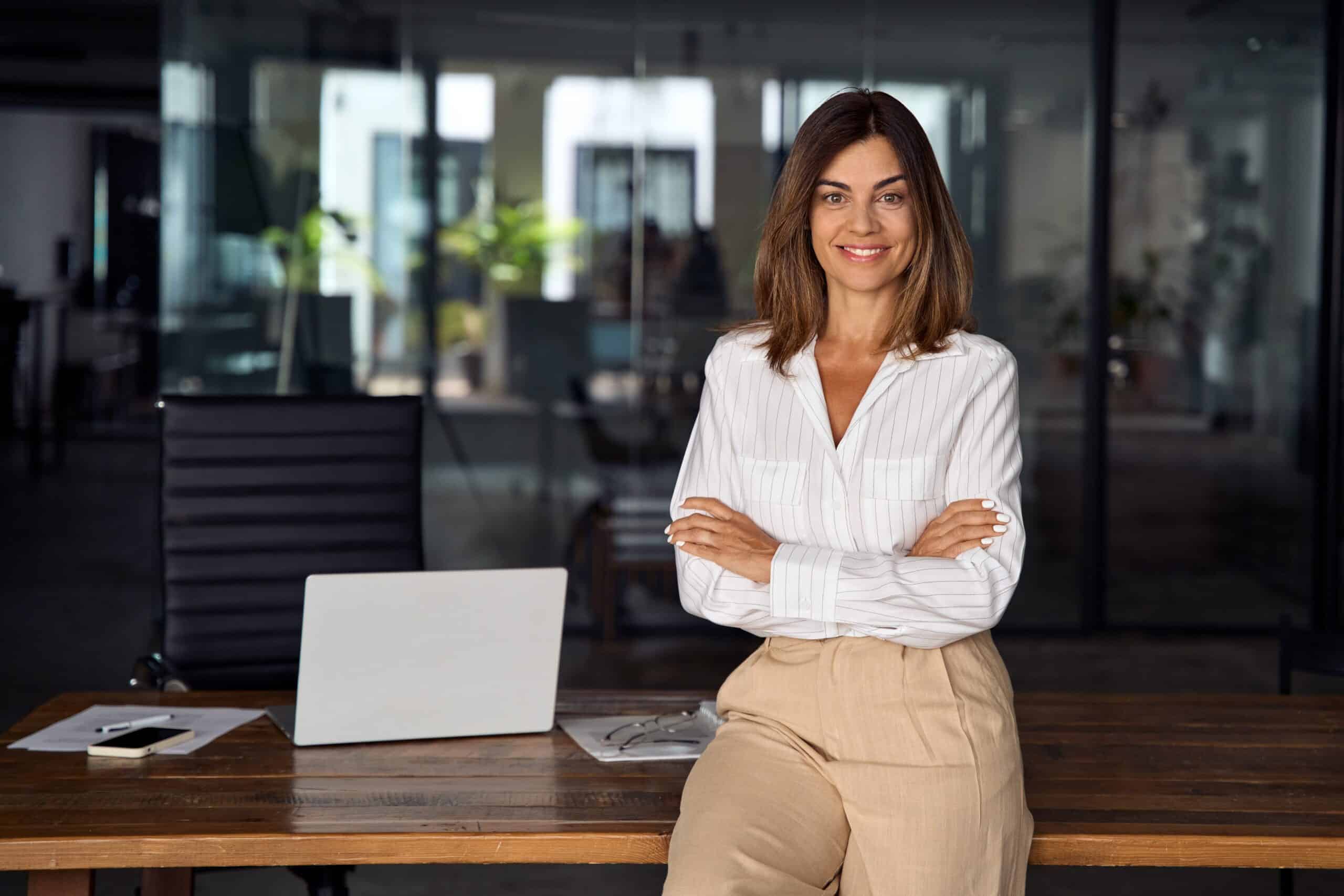 Beautiful Hispanic businesswoman leaning against desk and crossing arms