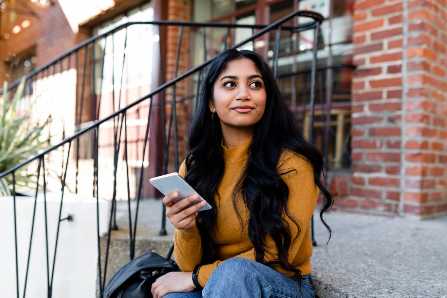 Working with TRS International Beautiful young woman sits outdoors on steps and checks her smartphone.