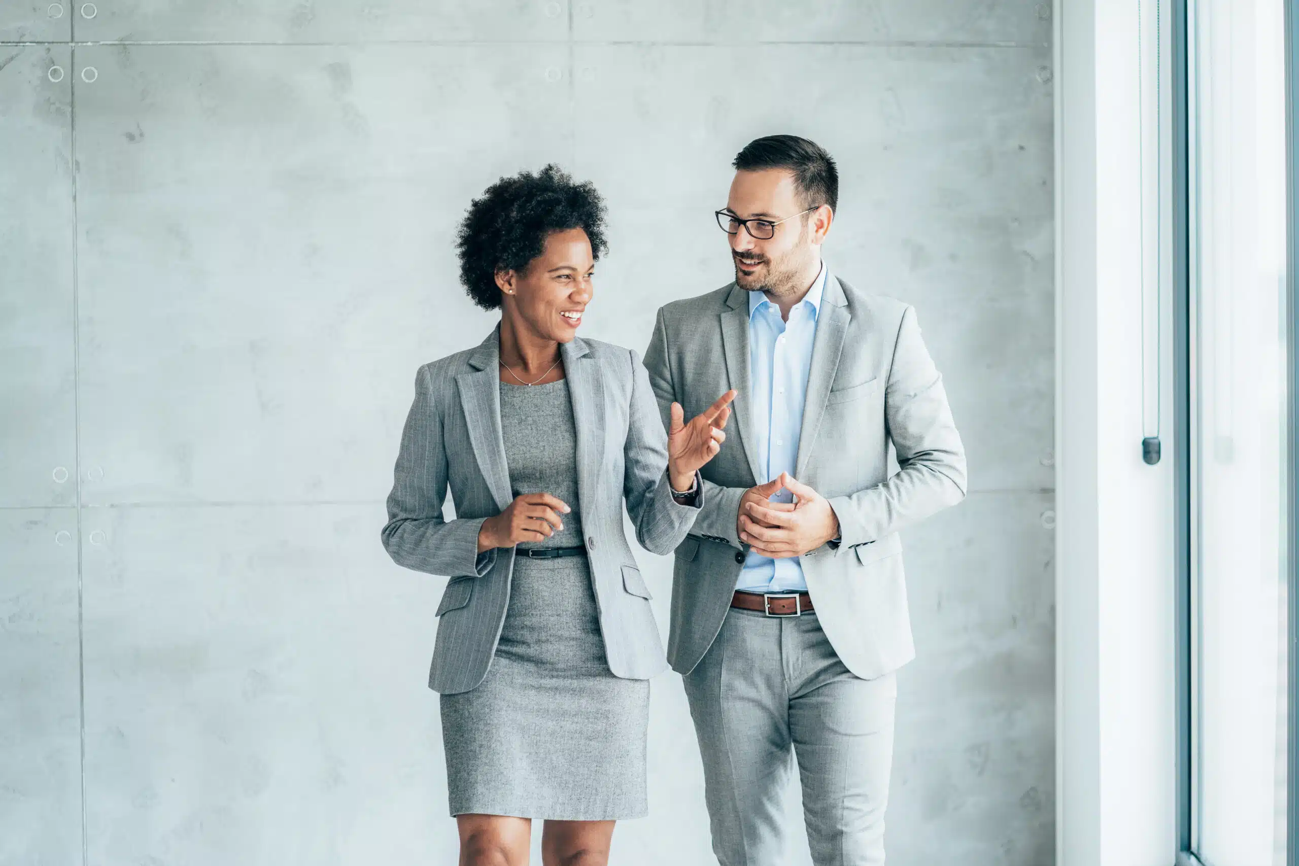Two smiling business people walking through office hall and talking