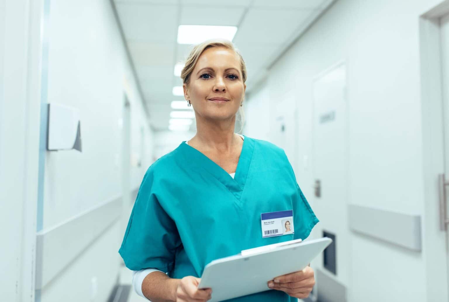 Portrait of mature female nurse working in hospital. Woman healthcare worker with clipboard in corridor.