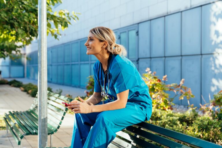 Young female nurse in scrubs sitting on a bench outdoors