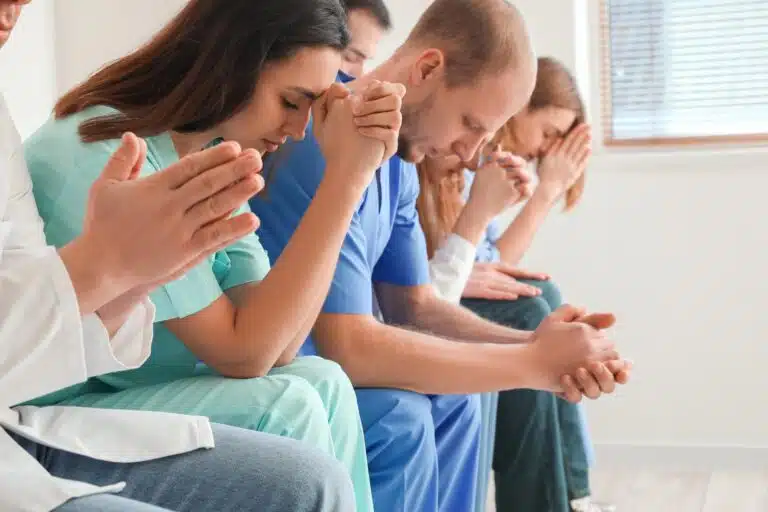 Line of doctors, nurses, and other healthcare providers praying