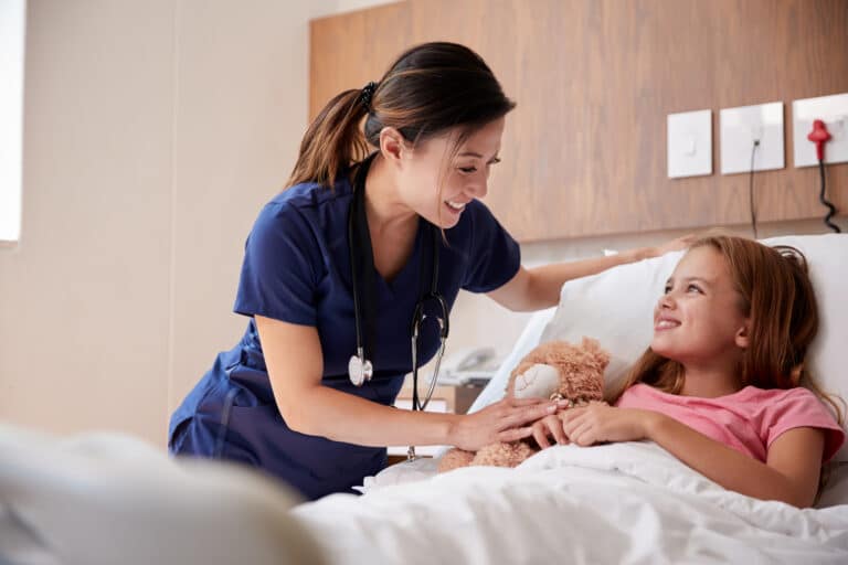 Female nurse visiting girl lying in hospital bed