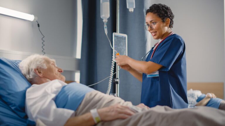 Hospital ward: friendly female head nurse making rounds does checkup on elderly patient resting in bed.