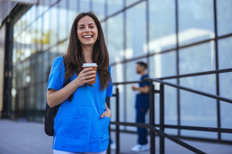 Portrait cute female healthcare worker breathing fresh air during lunch break, holding glass of coffee and looking at camera.