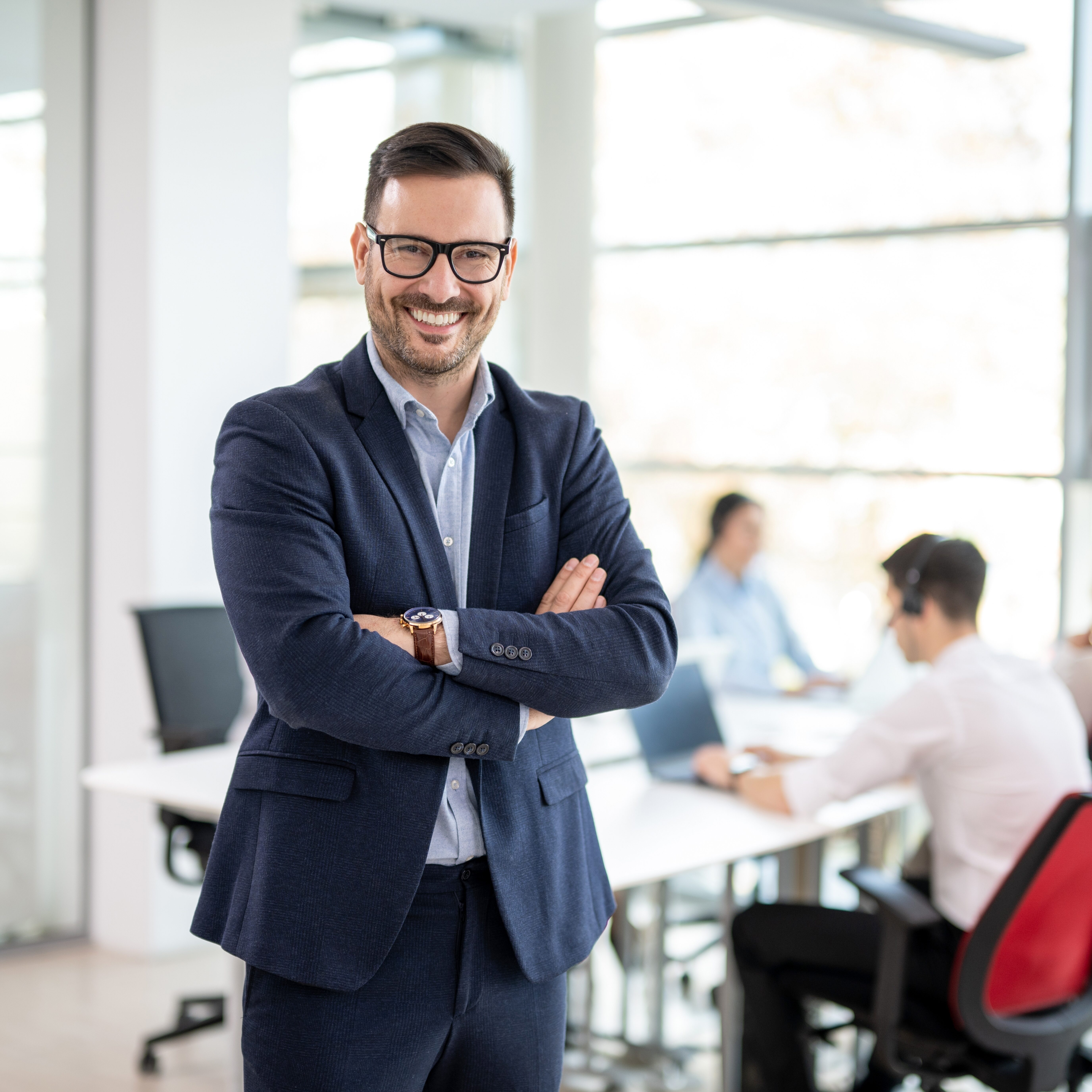 Leadership Team Confident businessman standing with crossed arms in front of a meeting room full of people