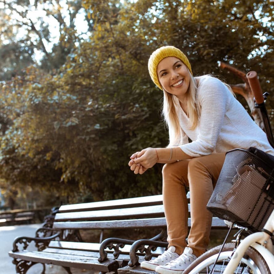 Travel Nursing Benefits with TRS Healthcare Young woman sitting on park bench next to parked bicycle