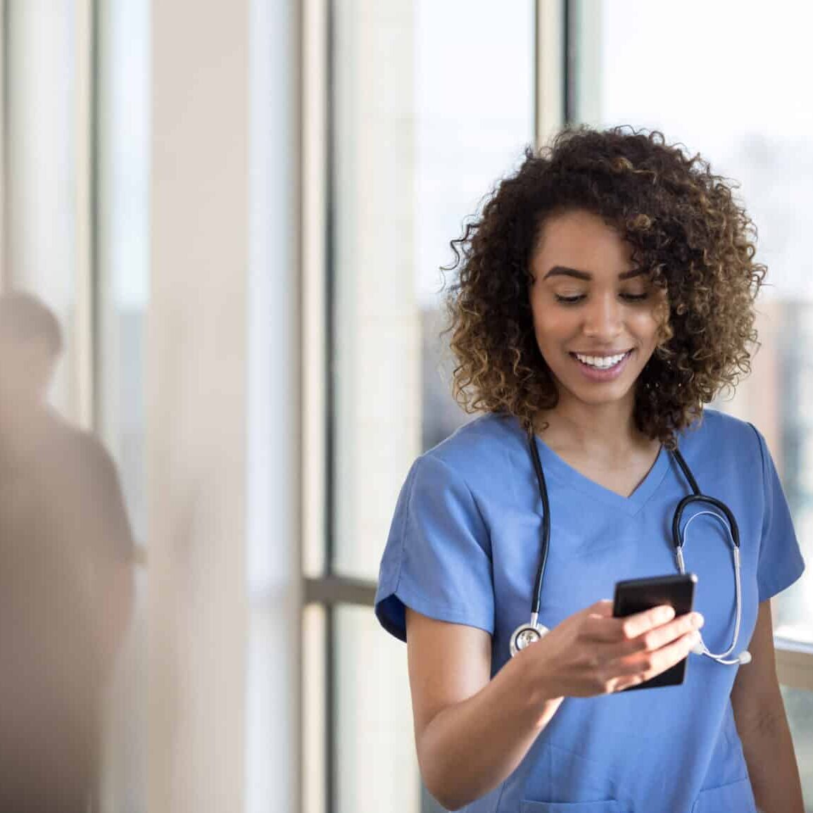 Travel Nursing Credentials with TRS Healthcare Attractive young female nurse checks smartphone as she walks in a hospital hallway